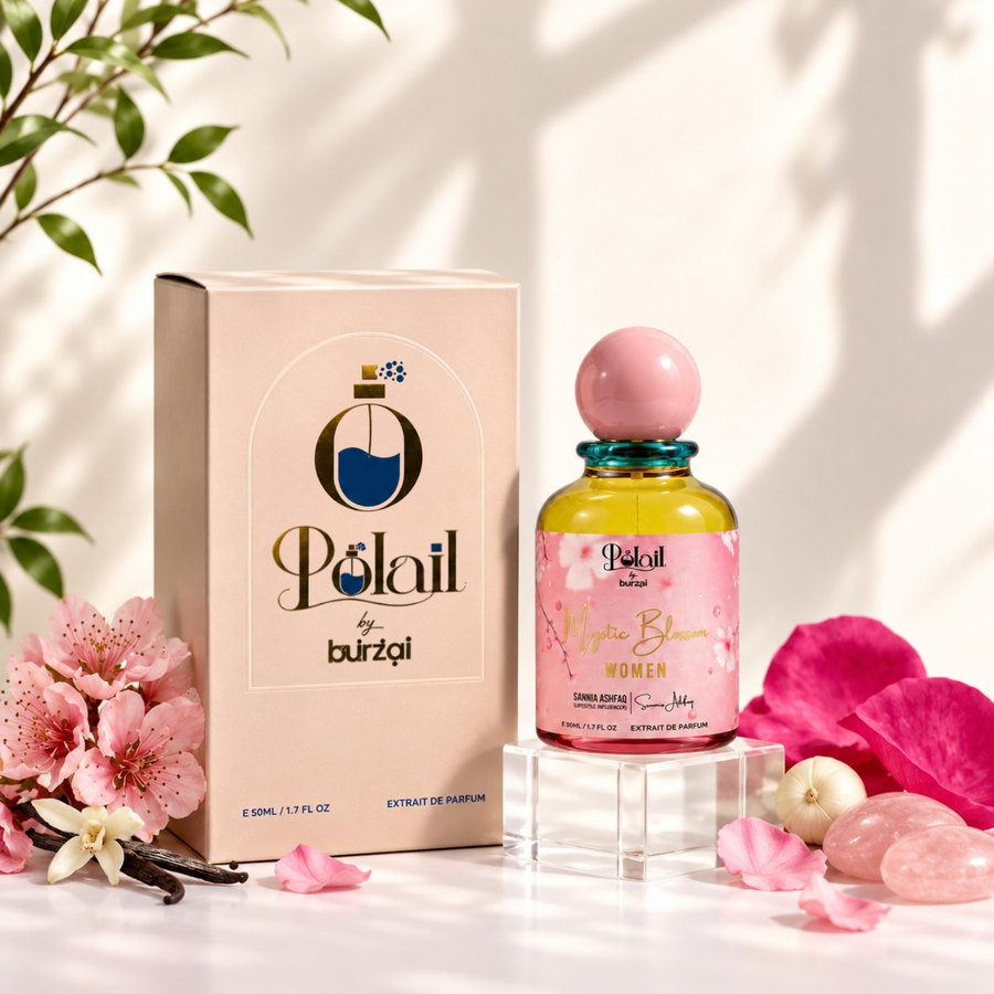 A bottle of'Polail by burzai Mystic Bloom' women perfume with a pink spherical cap and yellow liquid, displayed next to its beige packaging box on a white surface with pink flowers, rose petals, and soft leaf shadows.