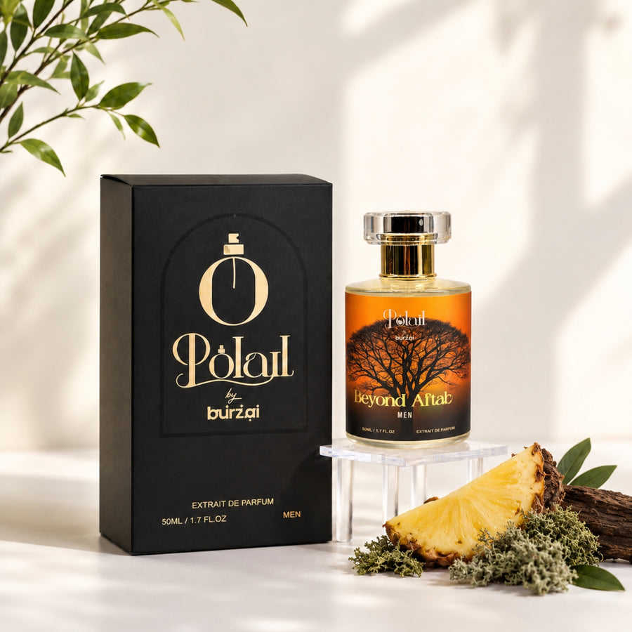 A bottle of polail by burzai beyond aftab Men perfume with amber liquid and a black box, styled on a white surface with a pineapple slice, greenery, and soft leaf shadows.