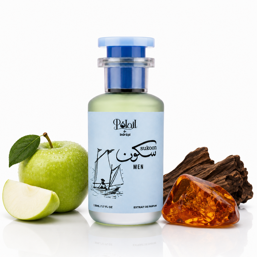 A bottle of sukoon perfume for men centered on a white background, flanked by a green apple on the left and a piece of wood and amber crystal on the right. The bottle has a light blue label and a blue cap.
